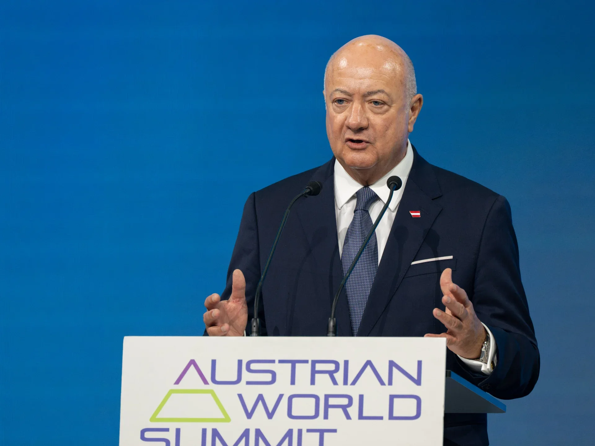 Christian Stocker duke folur para mikrofonave në Austrian World Summit, me sfond blu.