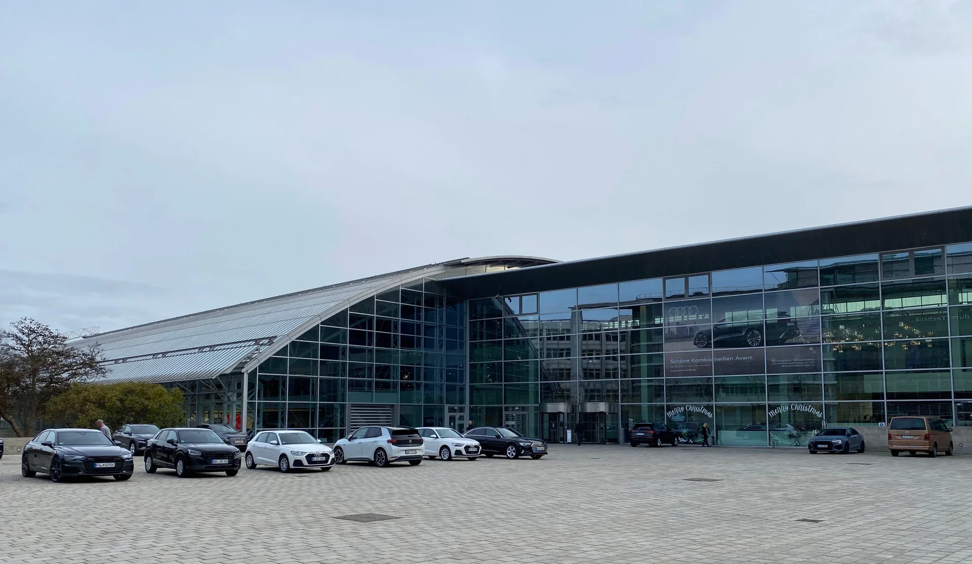 Ndërtesë me fasadë xhami dhe makina Audi të parkuara përpara, në Ingolstadt.